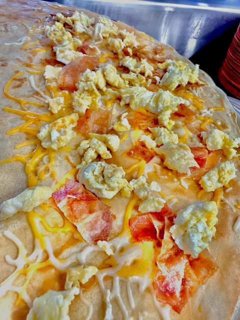 Breakfast crepe with scrambled eggs, bacon, and melted cheese